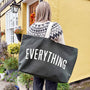 Person holding a black tote bag with 'EVERYTHING' text in front of a yellow building.