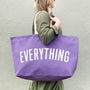 Person holding a purple tote bag with 'EVERYTHING' printed on it against a plain background