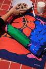 Colorful tablecloth with fruit design on a table with a bowl of cereal and glass of milk.