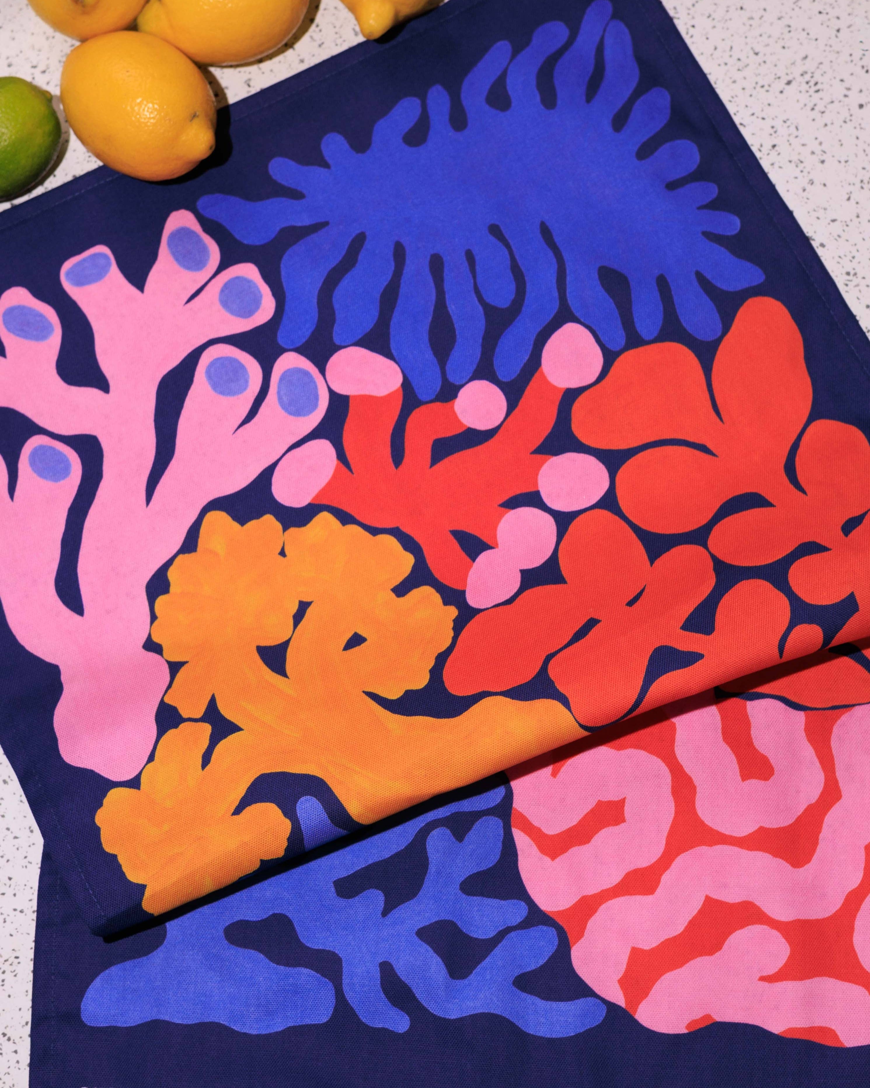 Colorful coral-patterned towel on a textured surface with lemons in the background