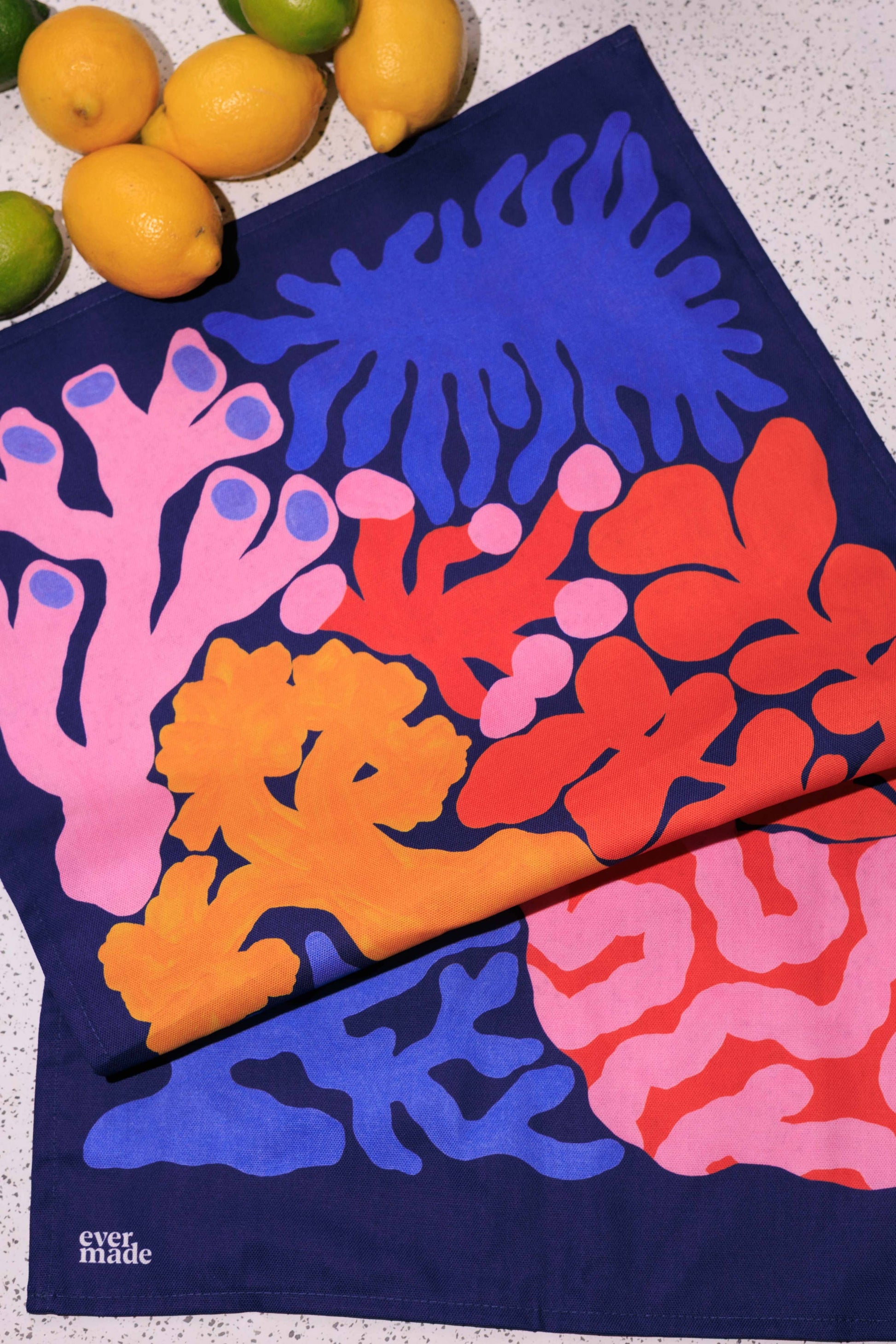 Colorful coral-patterned towel on a textured surface with lemons in the background