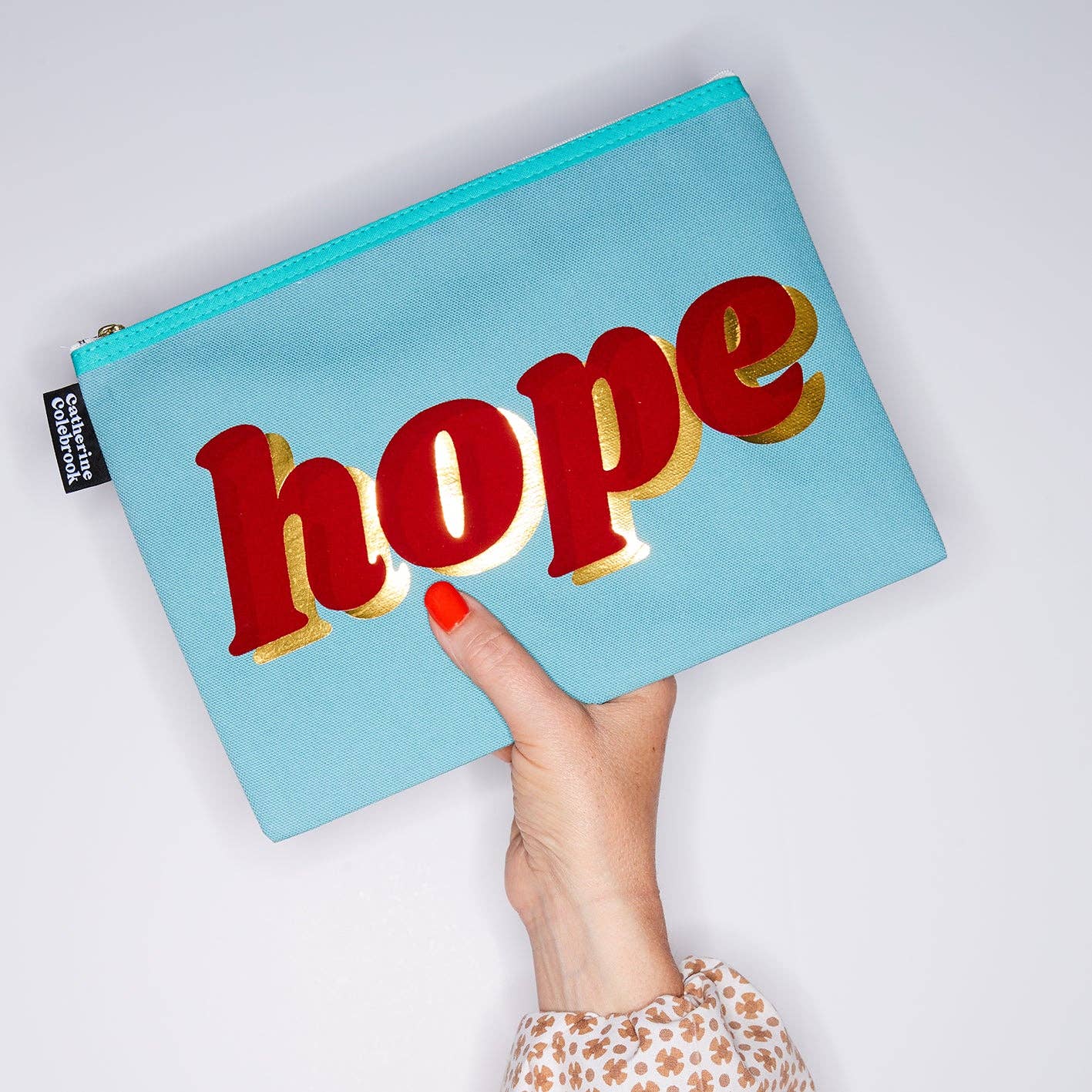 Light blue pouch with 'hope' text held by a hand on a white background