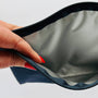 Hand with red nail polish opening a black zipper on a gray bag.
