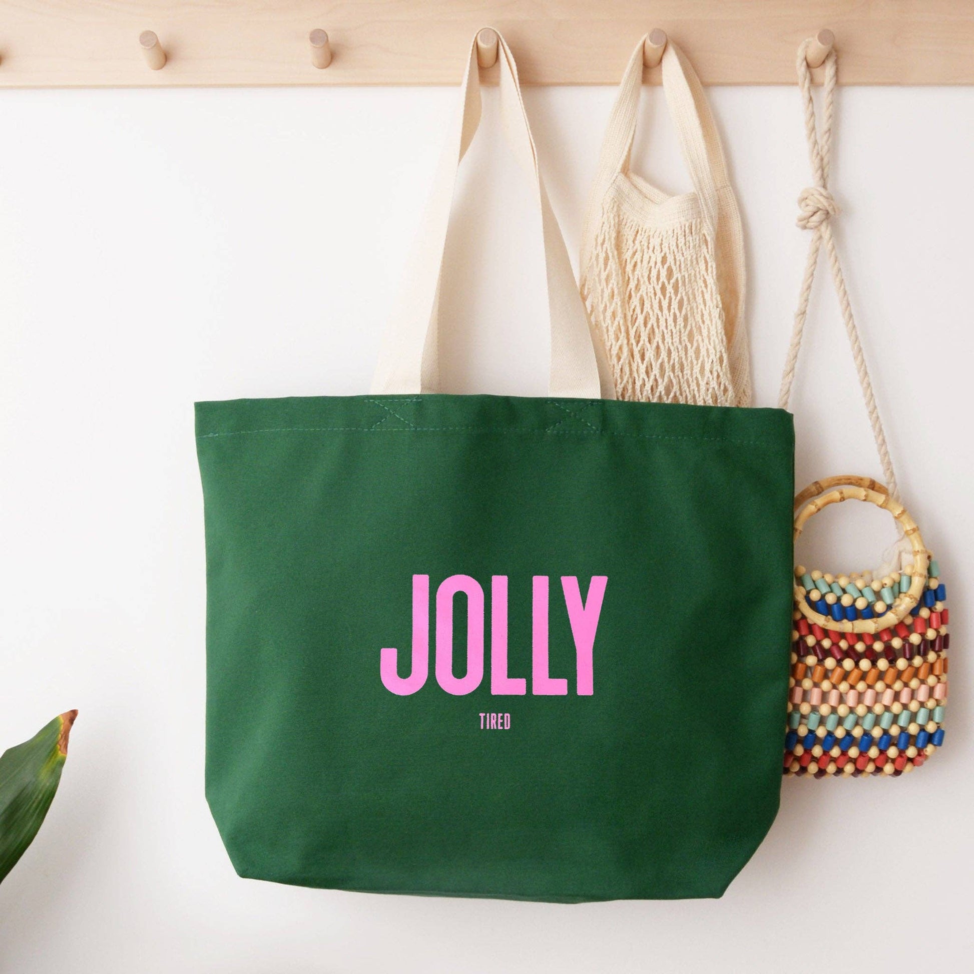 Green tote bag with 'Jolly' text, beige bag, and colorful woven bag on a white surface.