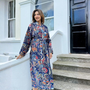 Woman wearing a floral robe standing on steps outside a house.