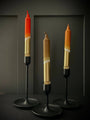 Three unique candles on stands against a dark background