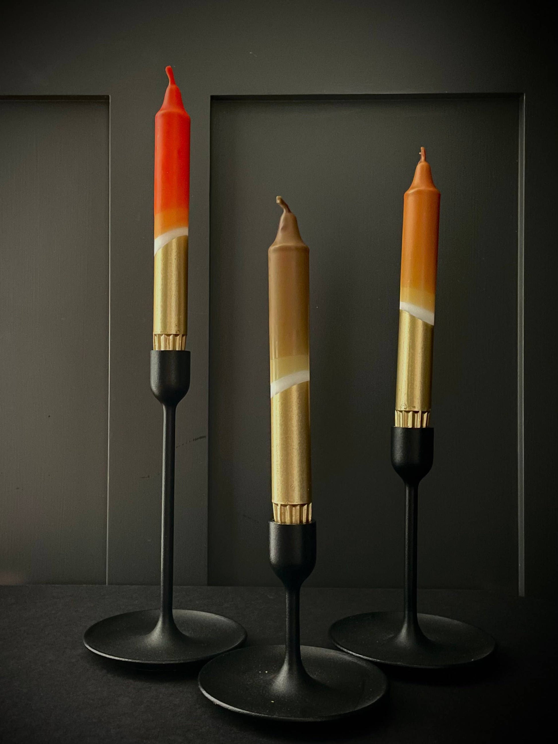 Three unique candles on stands against a dark background