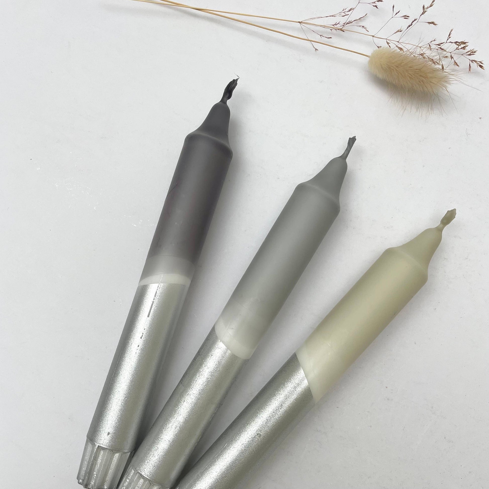 Three metallic markers on a light surface with dried plants.