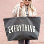 Person holding a black tote bag with 'EVERYTHING' printed on it against a pink background