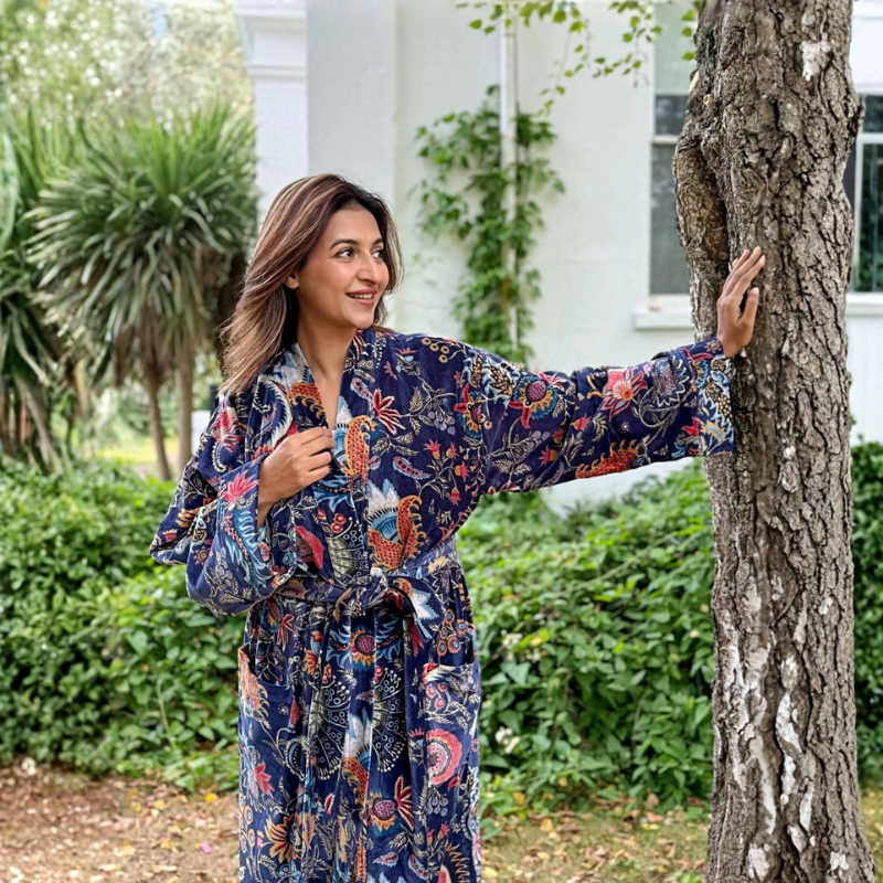Woman in a floral robe standing next to a tree in a garden setting