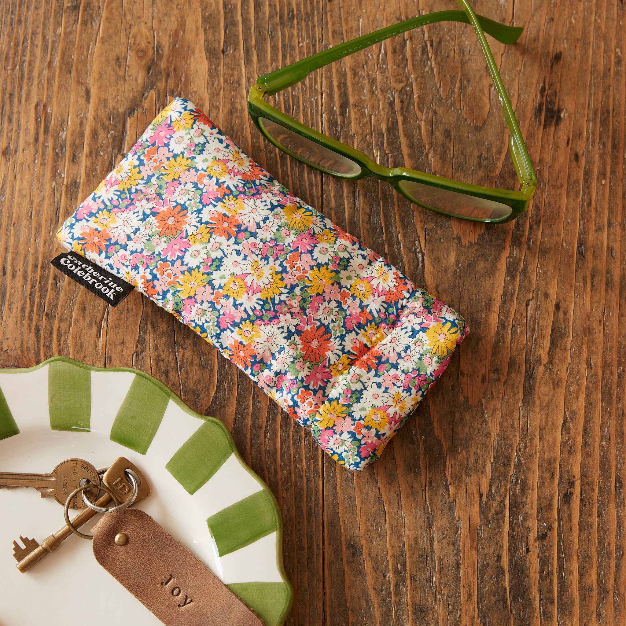 Floral eyeglass case on a wooden surface with keys and a dish.