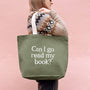Person holding a green tote bag with 'Can I go read my book?' text on a pink background