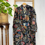 Colorful patterned robe hanging on a wooden hanger against a white wall with a plant to the left.