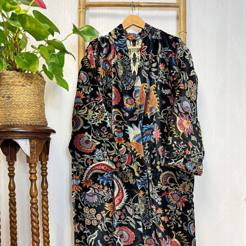 Colorful patterned robe hanging on a wooden hanger against a white wall with a plant to the left.