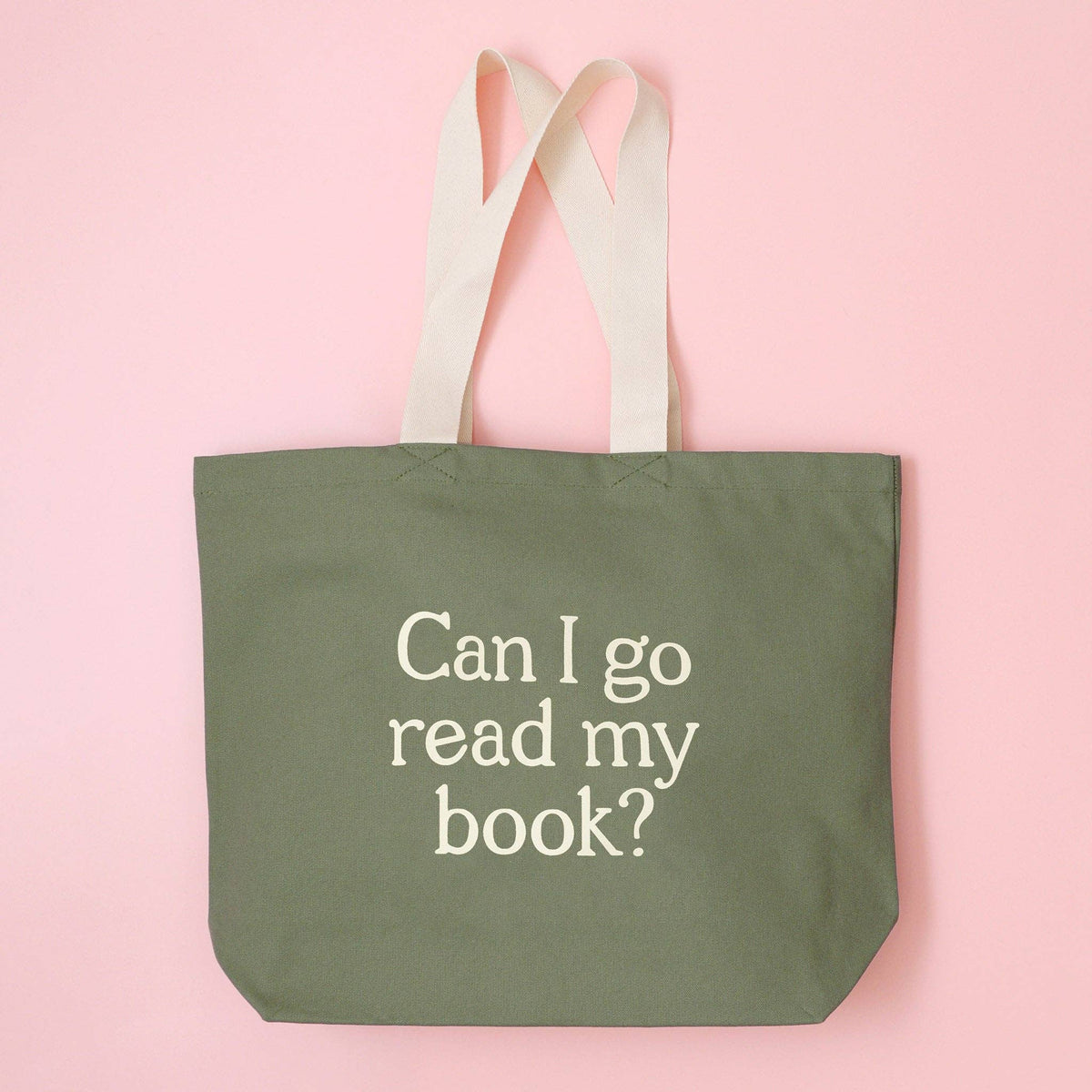Green tote bag with 'Can I go read my book?' text on a pink background