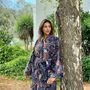 Woman in a floral dress standing next to a tree in a garden setting