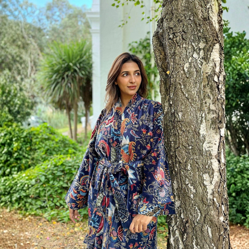 Woman in a floral dress standing next to a tree in a garden setting
