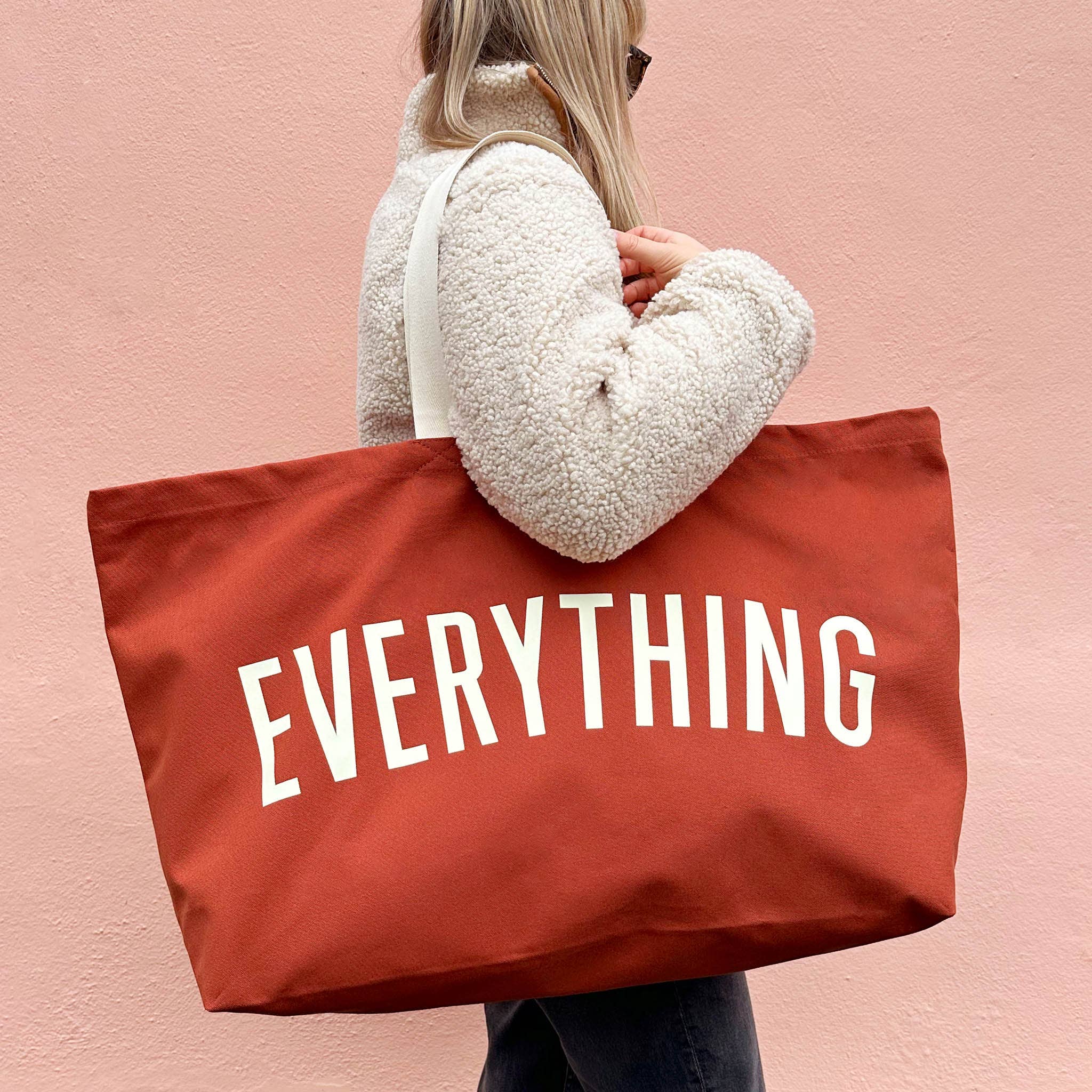 Person holding a red tote bag with 'EVERYTHING' text against a pink background