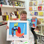 Person holding a framed artwork and a mug with a colorful design in a store setting.