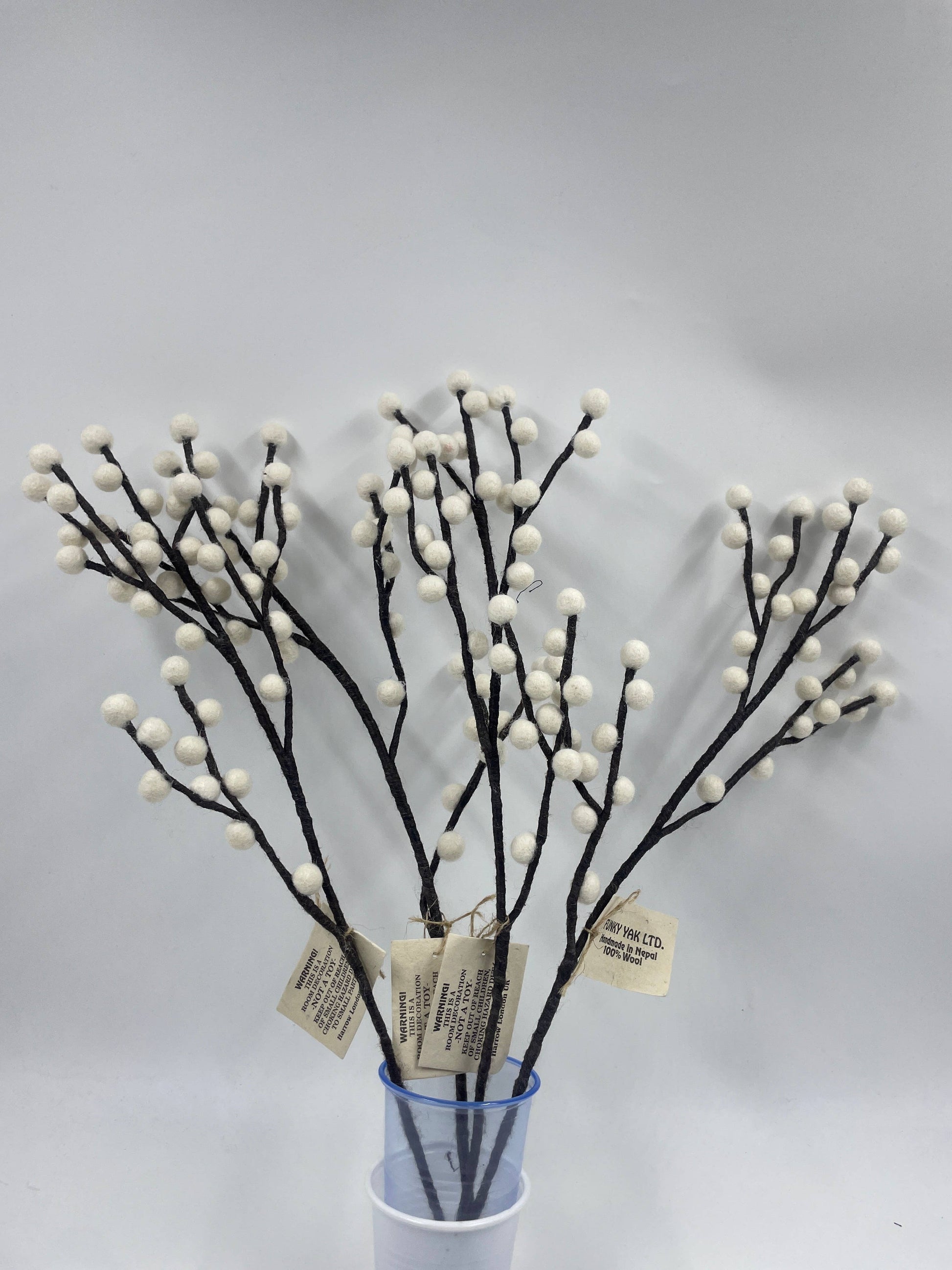 Decorative branches with white berries in a clear container on a light gray background
