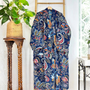 Floral-patterned garment hanging on a wooden hanger against a white wall with a plant and wooden table.