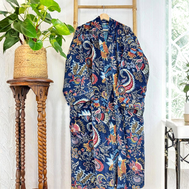 Floral-patterned garment hanging on a wooden hanger against a white wall with a plant and wooden table.