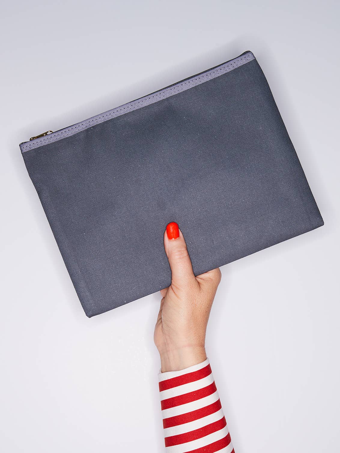Gray clutch held by a hand with red nail polish on a light gray background