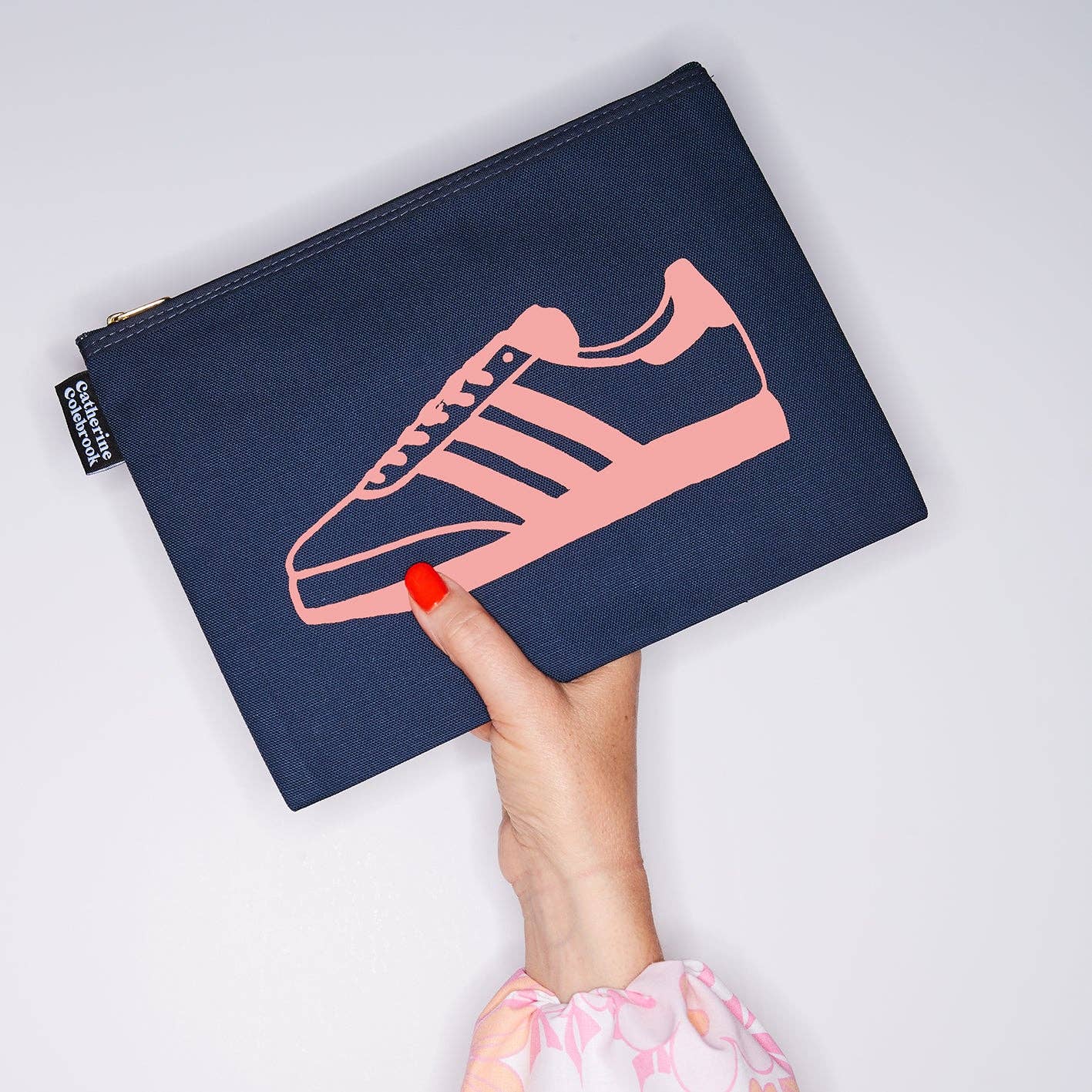 Navy pouch with pink sneaker design held by a hand against a light gray background