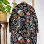 Colorful embroidered jacket on a hanger against a white wall with a plant in the corner.