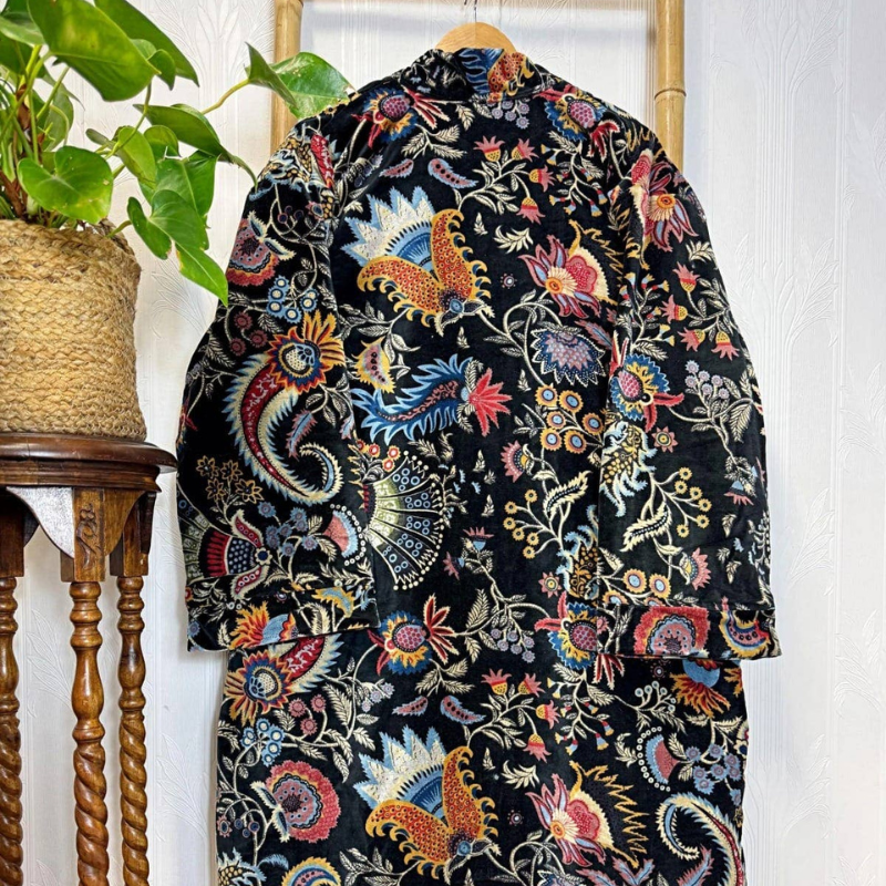 Colorful embroidered jacket on a hanger against a white wall with a plant in the corner.