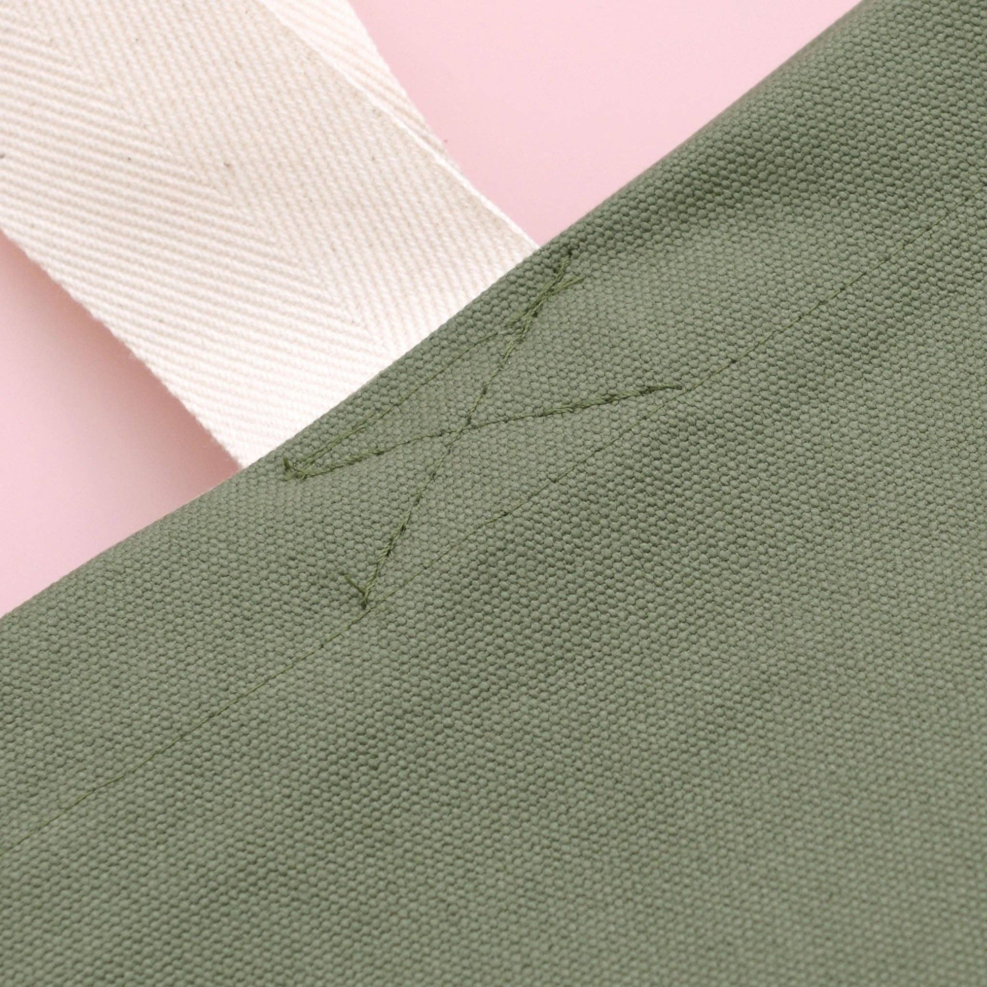 Close-up of green fabric with stitching detail on a pink background