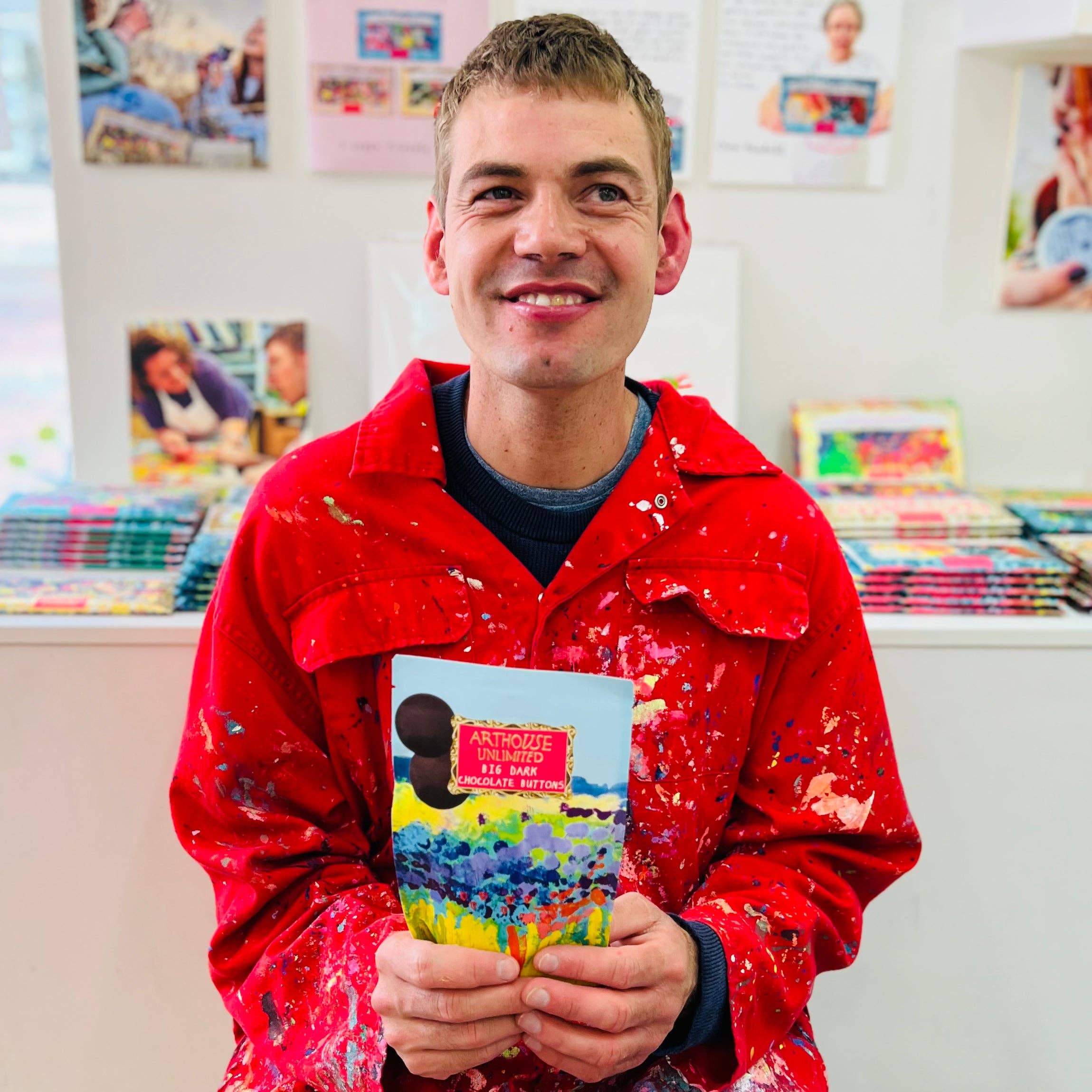 Person wearing a red jacket holding a colorful book in an indoor setting with shelves and books in the background.