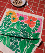 Floral patterned towel on a red checkered tablecloth with a bowl of cereal and spoon.