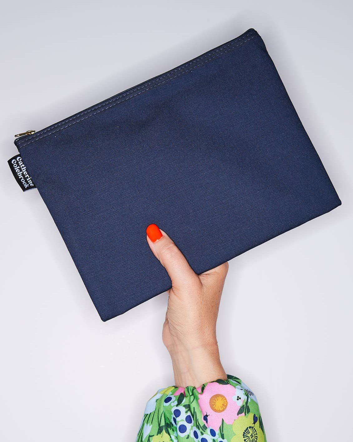 Navy blue pouch held by a hand with floral sleeve on a light gray background