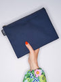 Navy blue pouch held by a hand with floral sleeve on a light gray background