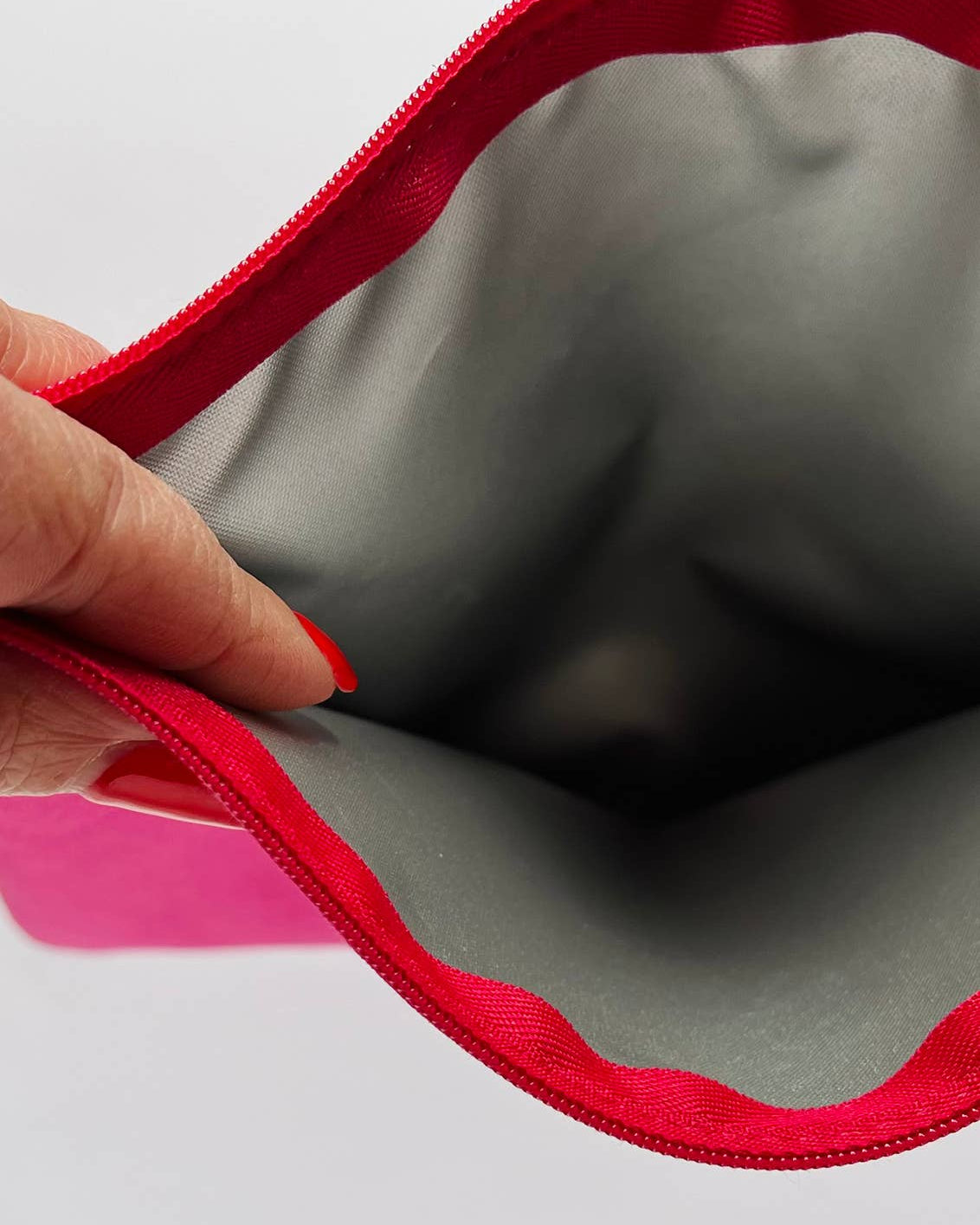 Gray pouch with red zipper held open by a hand on a white background