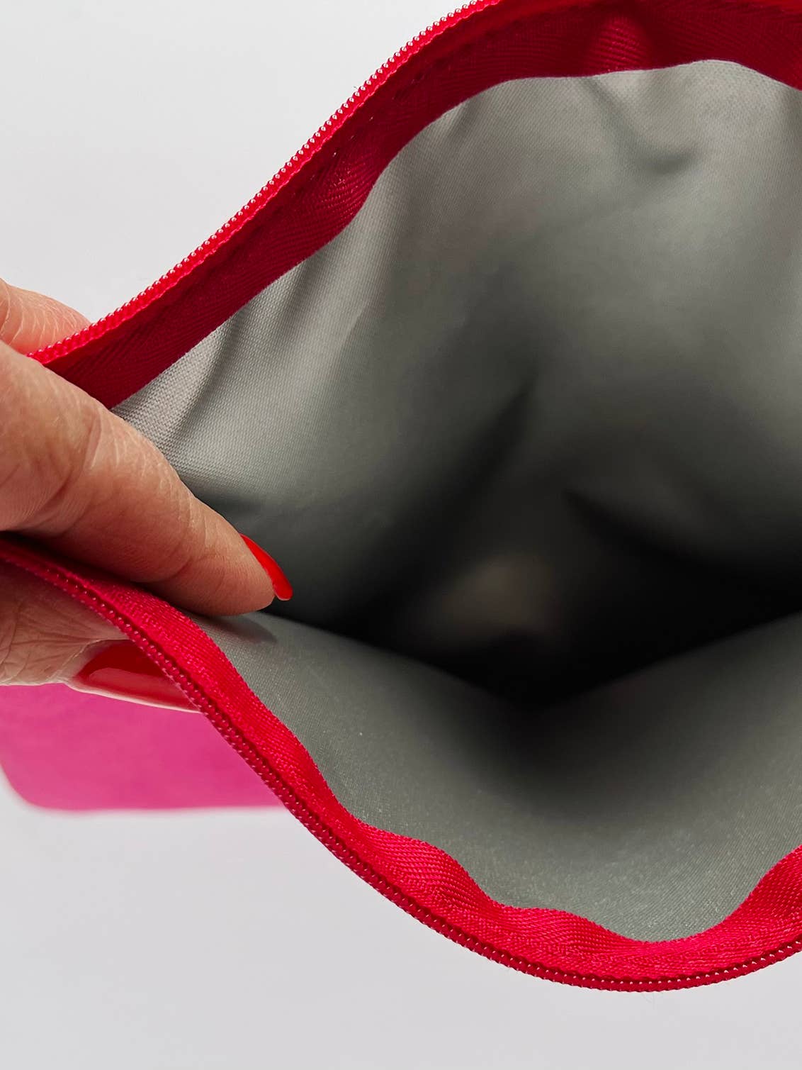 Gray pouch with red zipper held open by a hand on a white background