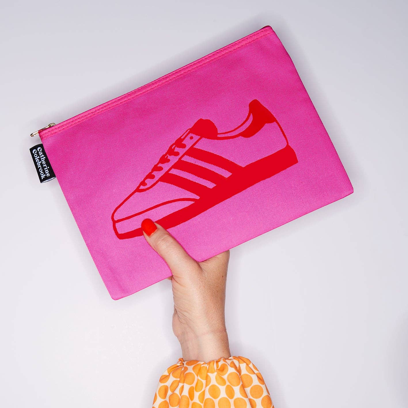Pink pouch with red shoe design held by a hand on a light gray background