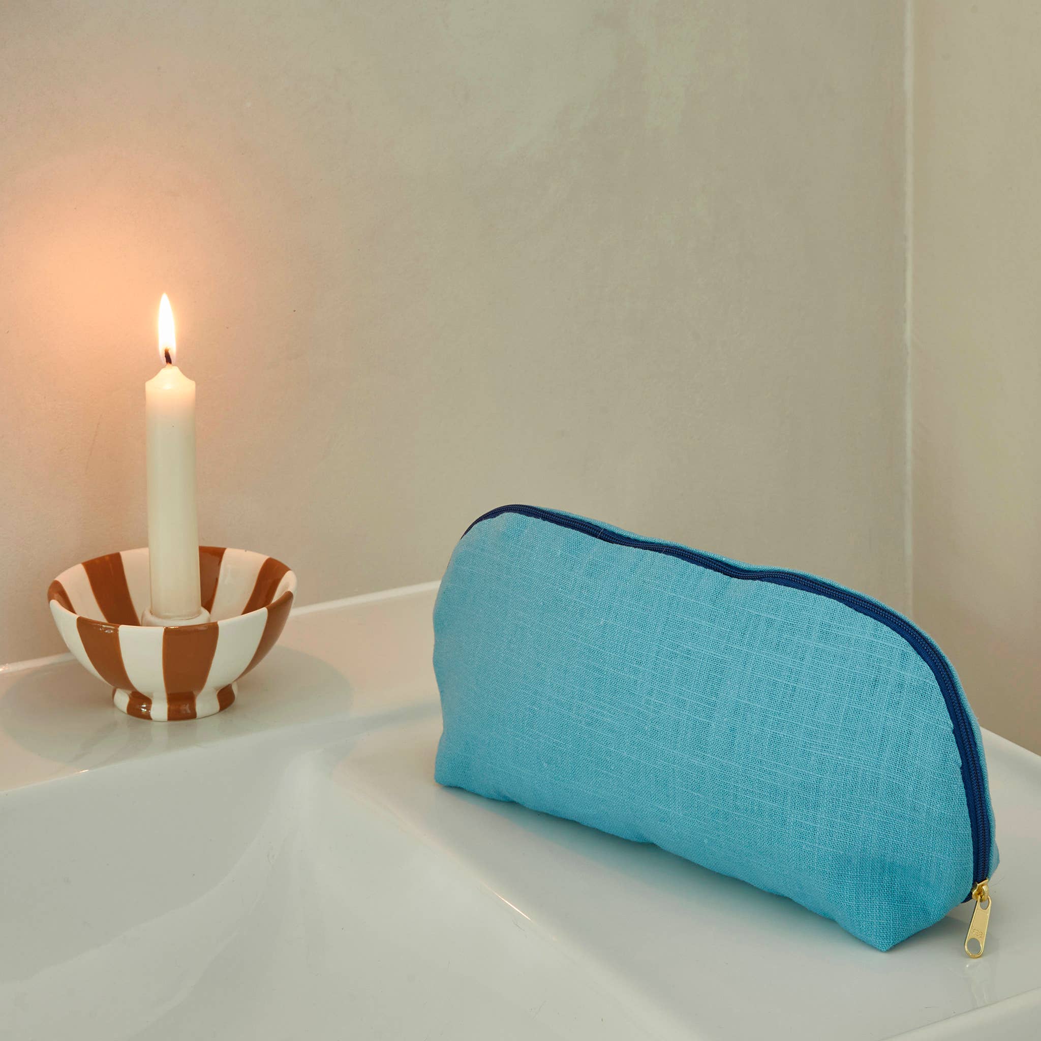 Blue pouch on a white surface with a candle in the background