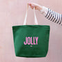 Green tote bag with 'JOLLY' text held by a person against a pink background