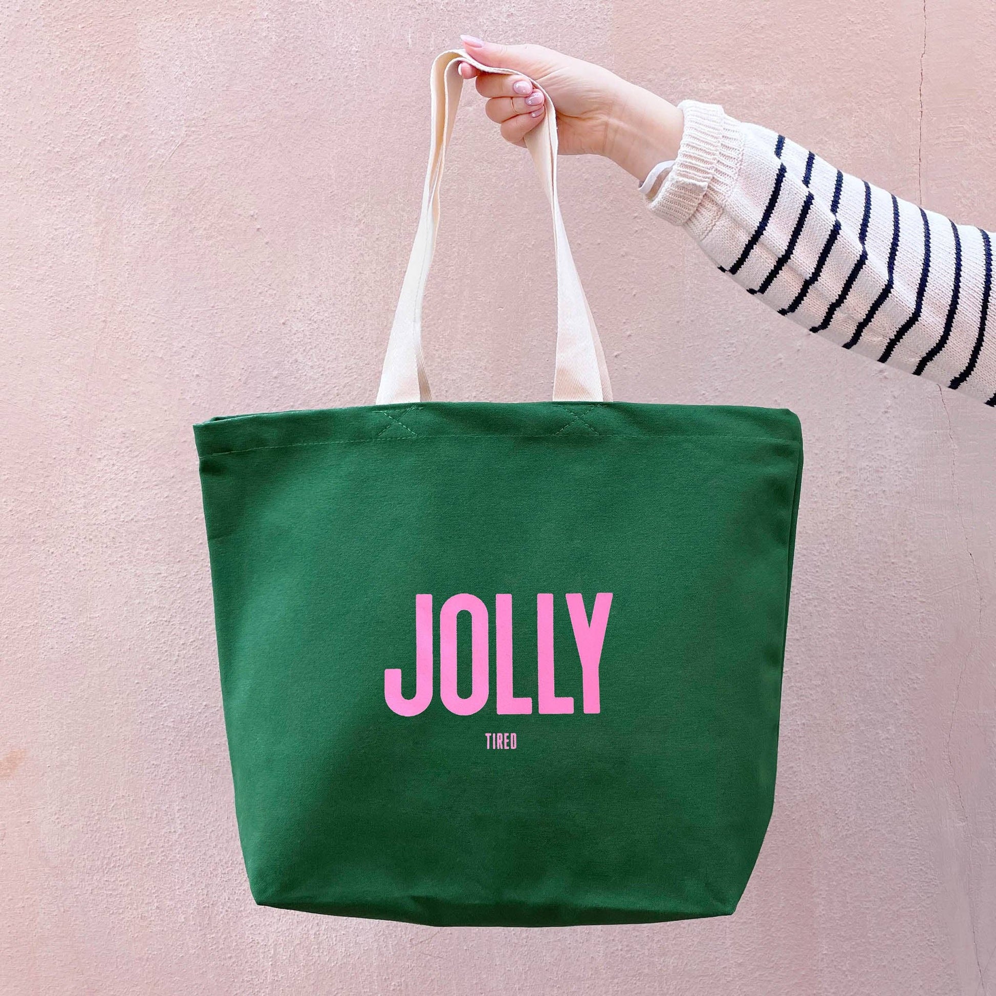 Green tote bag with 'JOLLY' text held by a person against a pink background