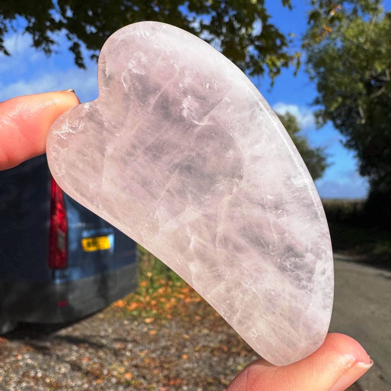 Heart-shaped crystal held by a hand with a car and trees in the background