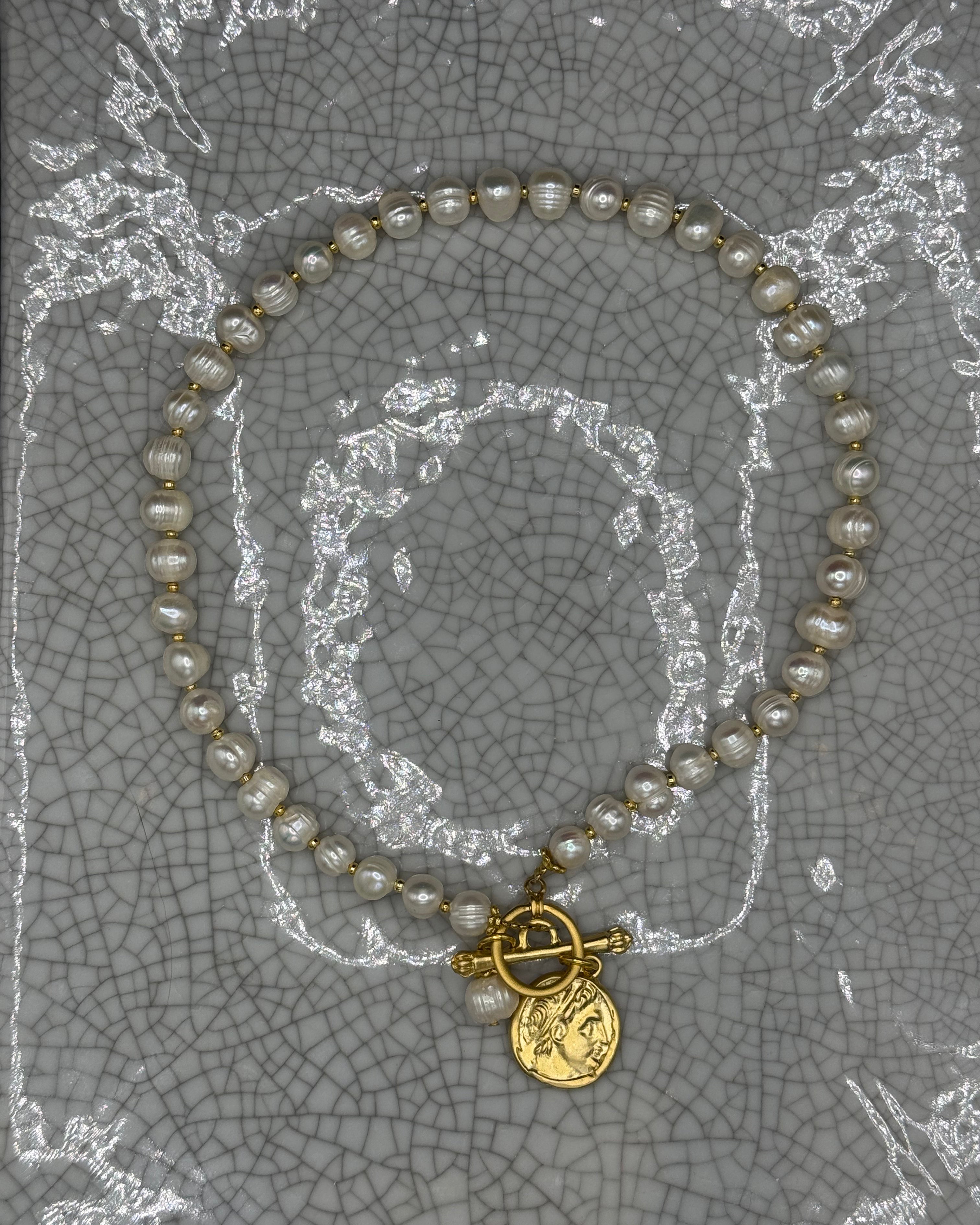 Full view of freshwater pearl necklace with gold Roman coin and T-bar clasp laid flat