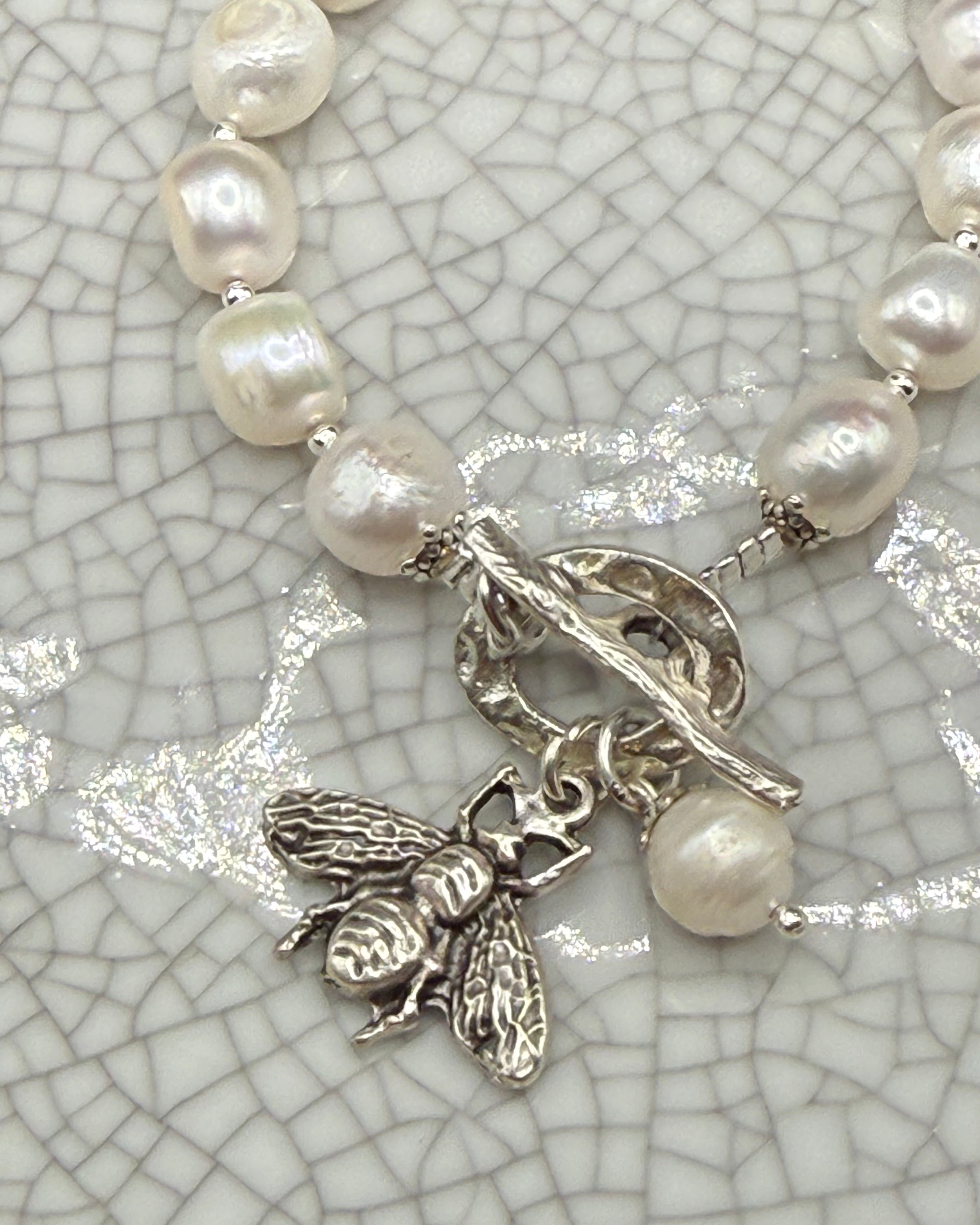 Close-up of silver bee charm and freshwater pearl drop on handmade pearl bracelet
