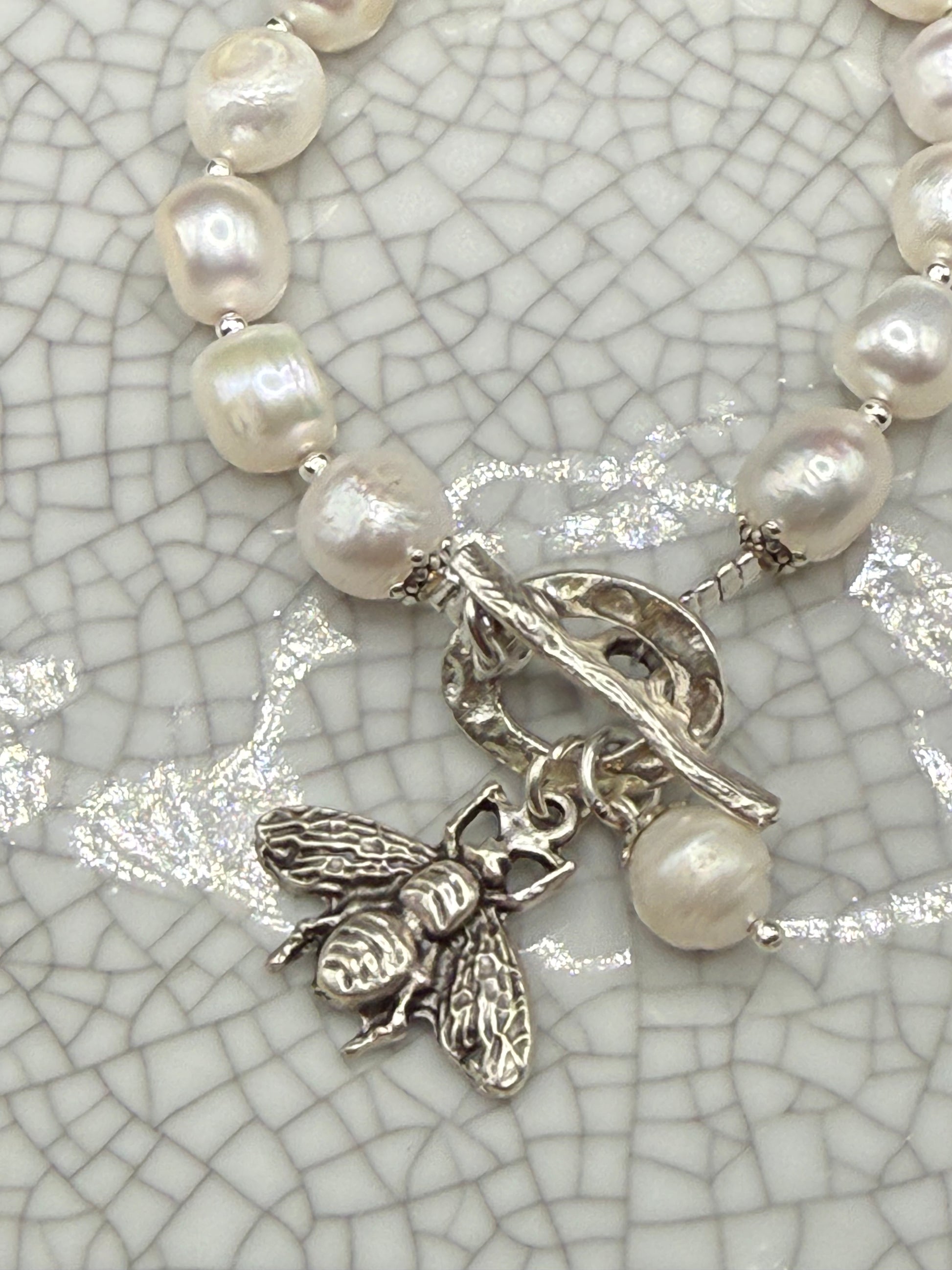 Close-up of silver bee charm and freshwater pearl drop on handmade pearl bracelet