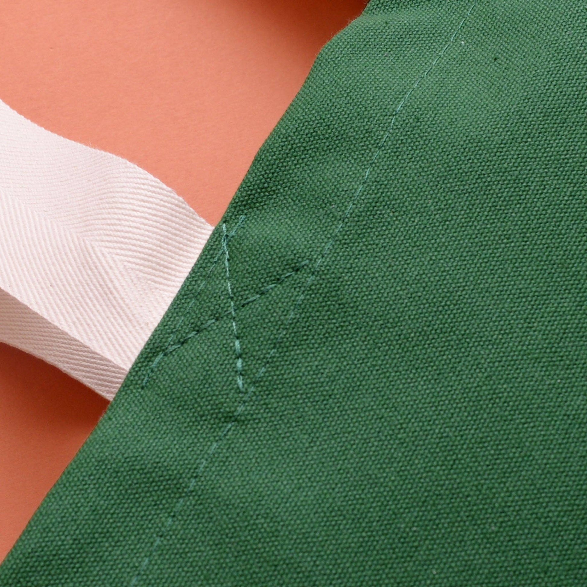 Close-up of green fabric with white stitching on a peach background