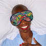 Person wearing a colorful floral sleep mask with a white pillow and blue shirt in the background.