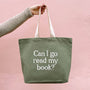 Green tote bag with 'Can I go read my book?' text held by a person against a pink background