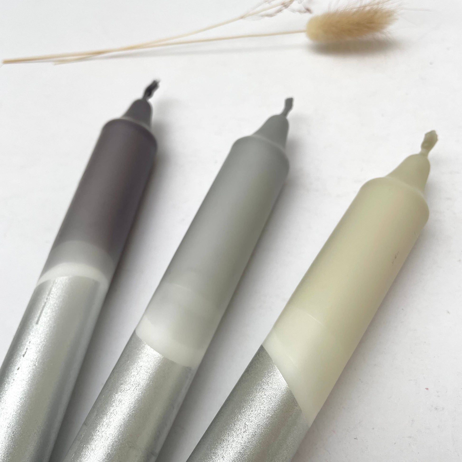 Three metallic markers on a white surface with dried plants in the background