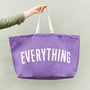Purple tote bag with 'EVERYTHING' text held by a person against a light green background